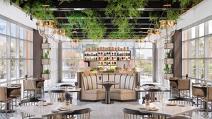 A modern restaurant with a central seating area, large windows, and hanging greenery.