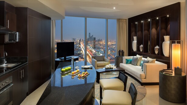 A modern living room with a city view, a kitchen with a microwave, and a dining area with a glass table.