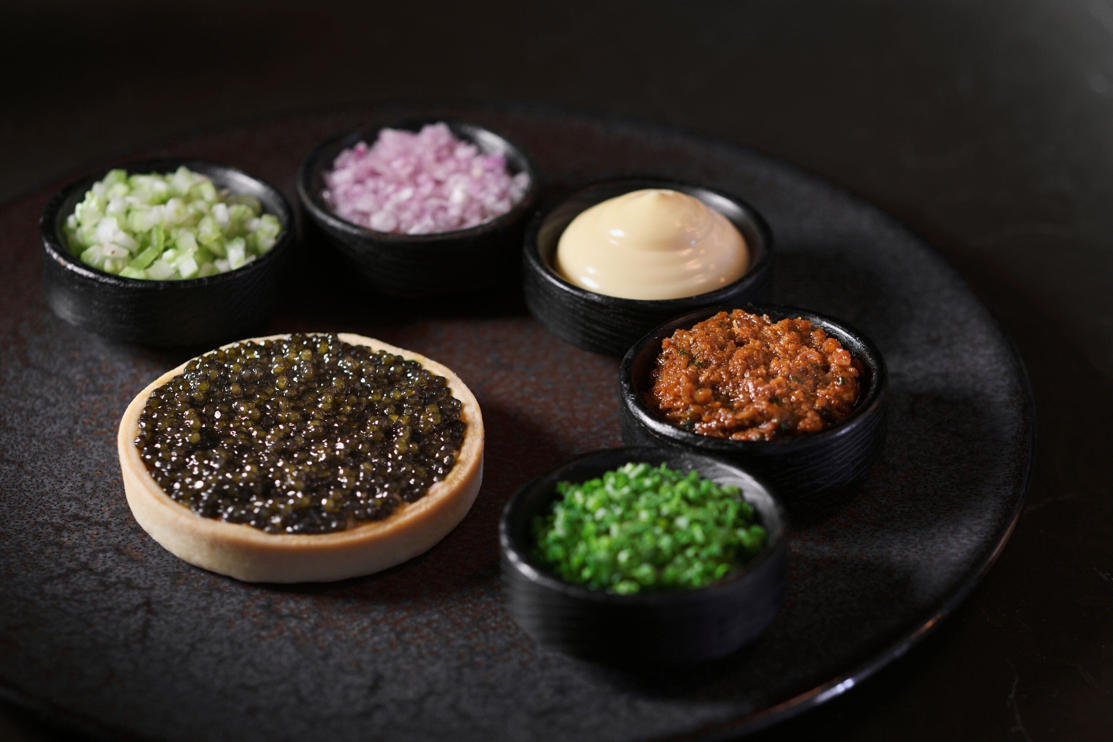 A plate with various condiments including caviar, chopped onions, and green peas.
