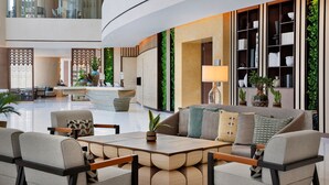 A spacious lobby with a reception desk, seating area, and indoor plants.
