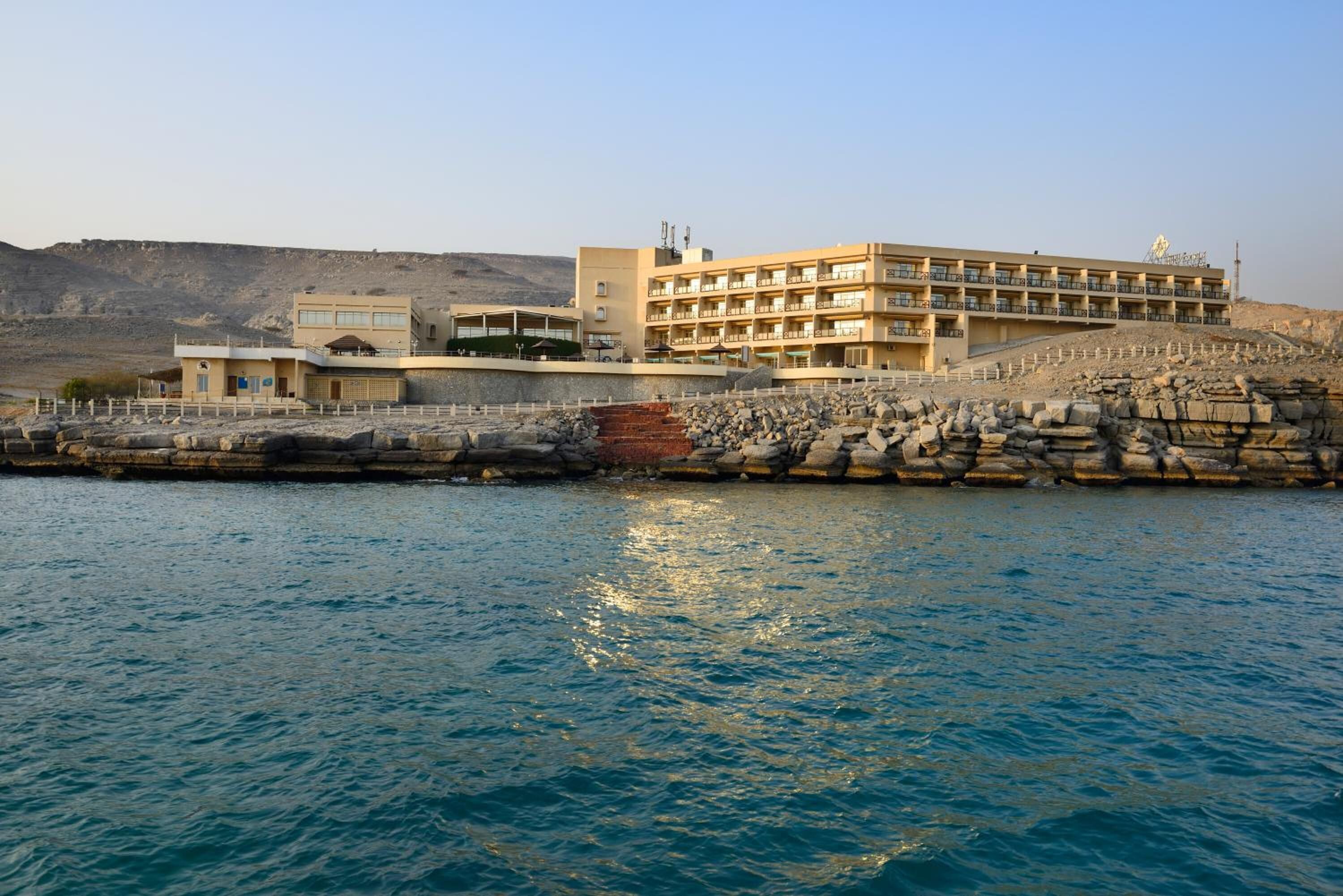 Un hotel frente al mar con varios pisos, una costa rocosa y vistas despejadas al océano.