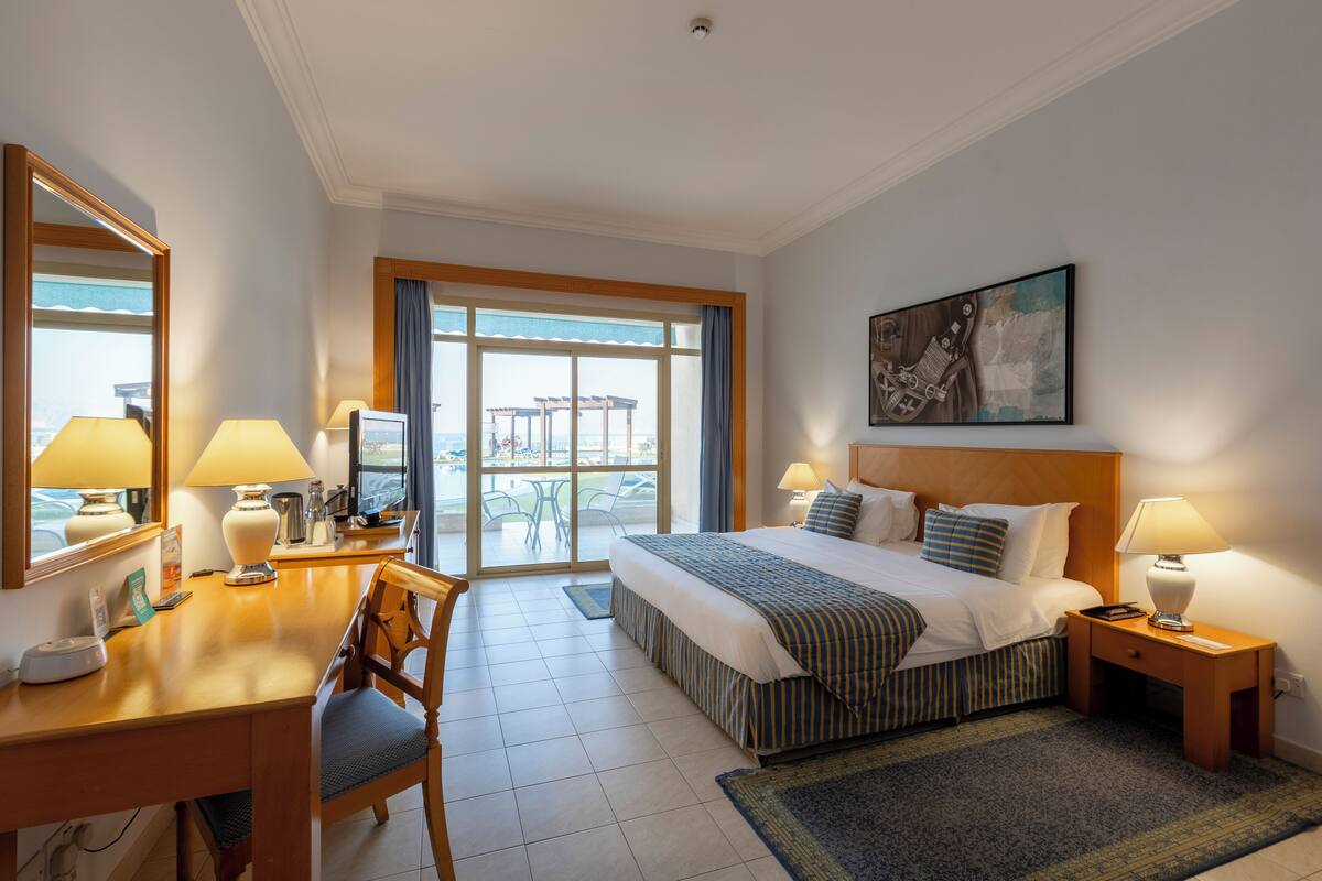 A hotel room with a bed, desk, chair, and a large window offering a view.