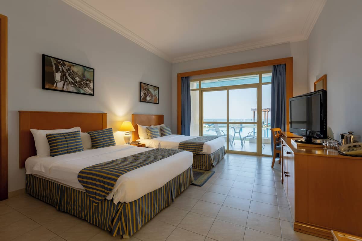 A hotel room with two beds, a TV, a desk, and a balcony with a view.