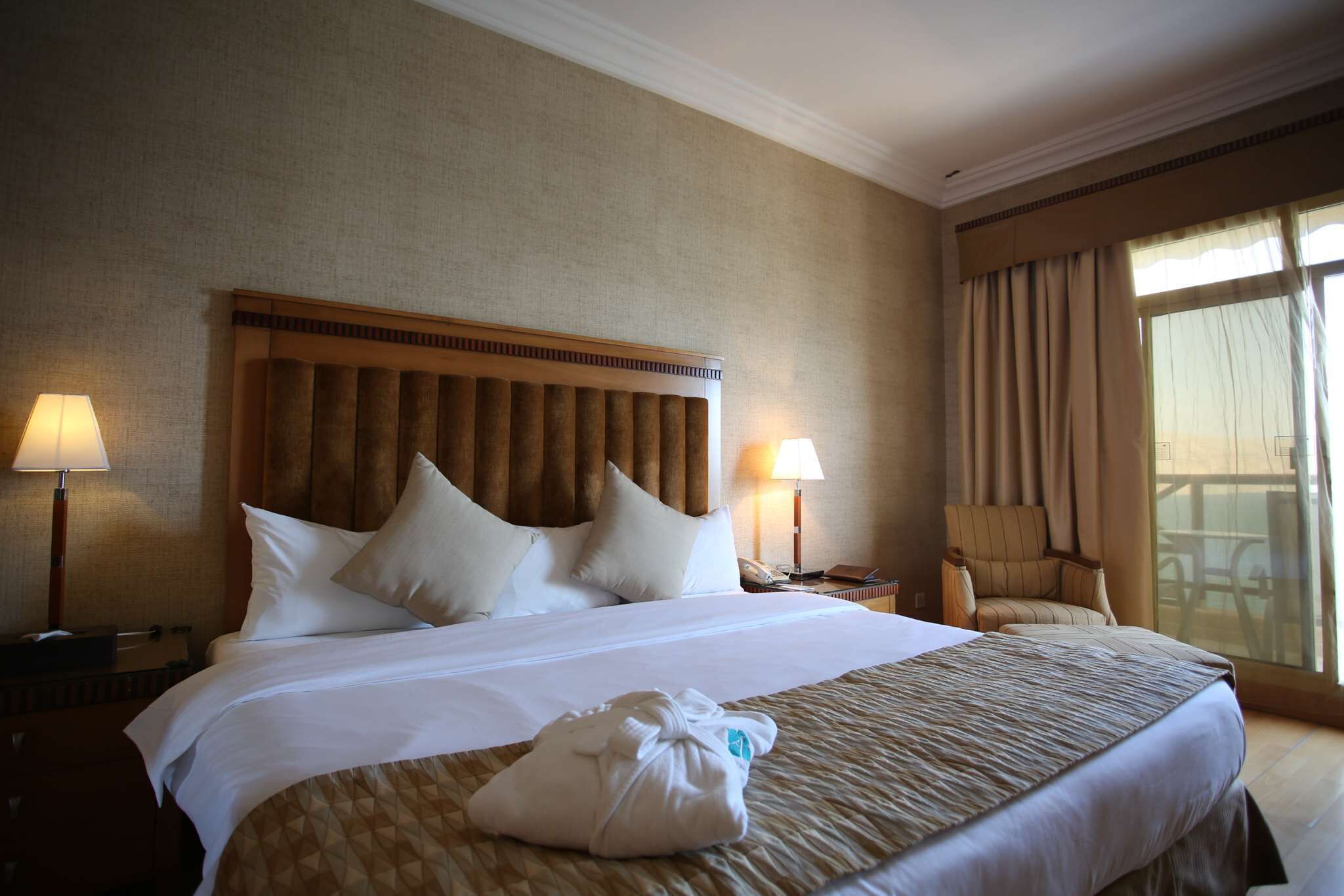 A hotel room with a large bed, two bedside lamps, a chair, and a window with curtains.