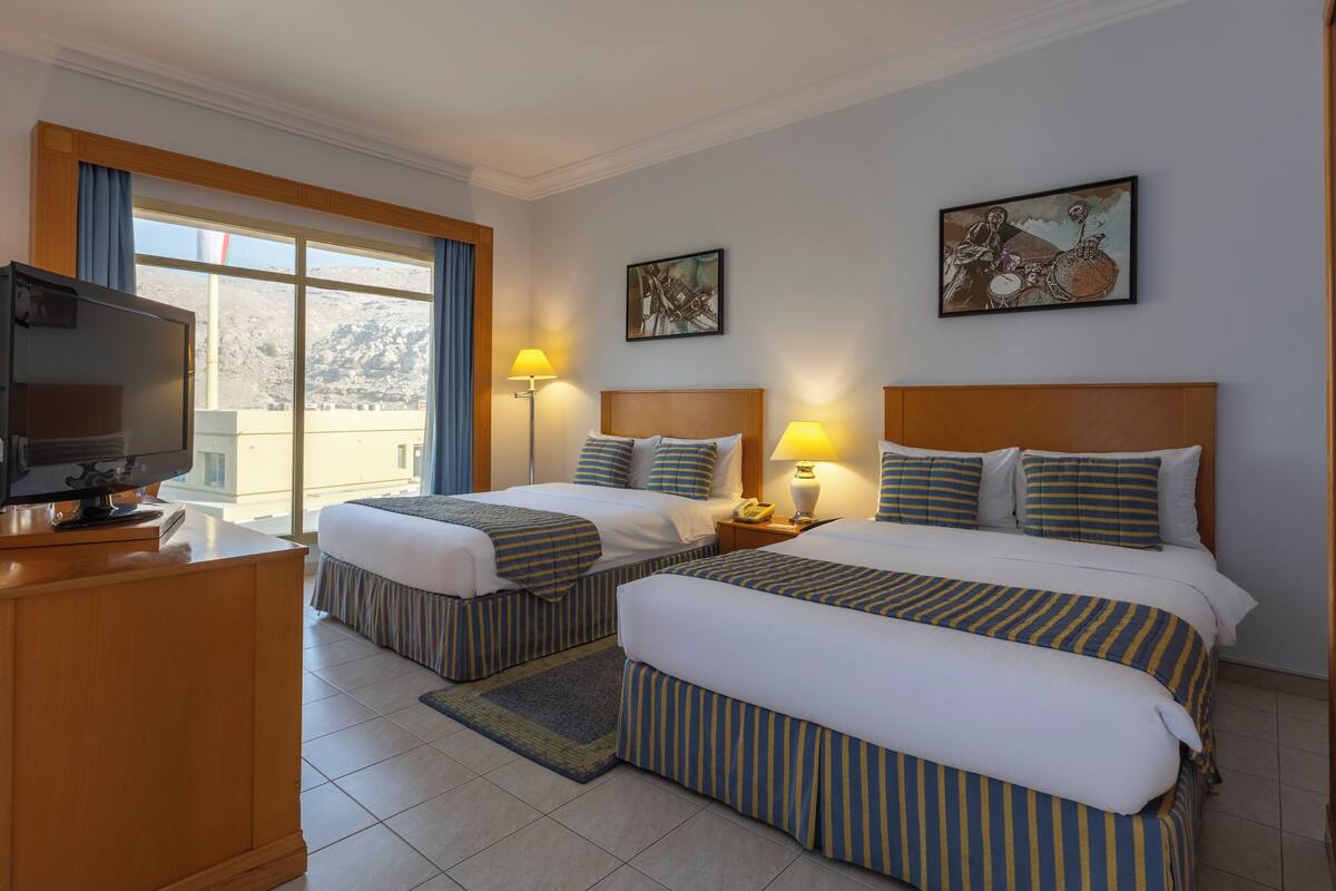 A hotel room with two beds, a TV, and artwork on the walls.