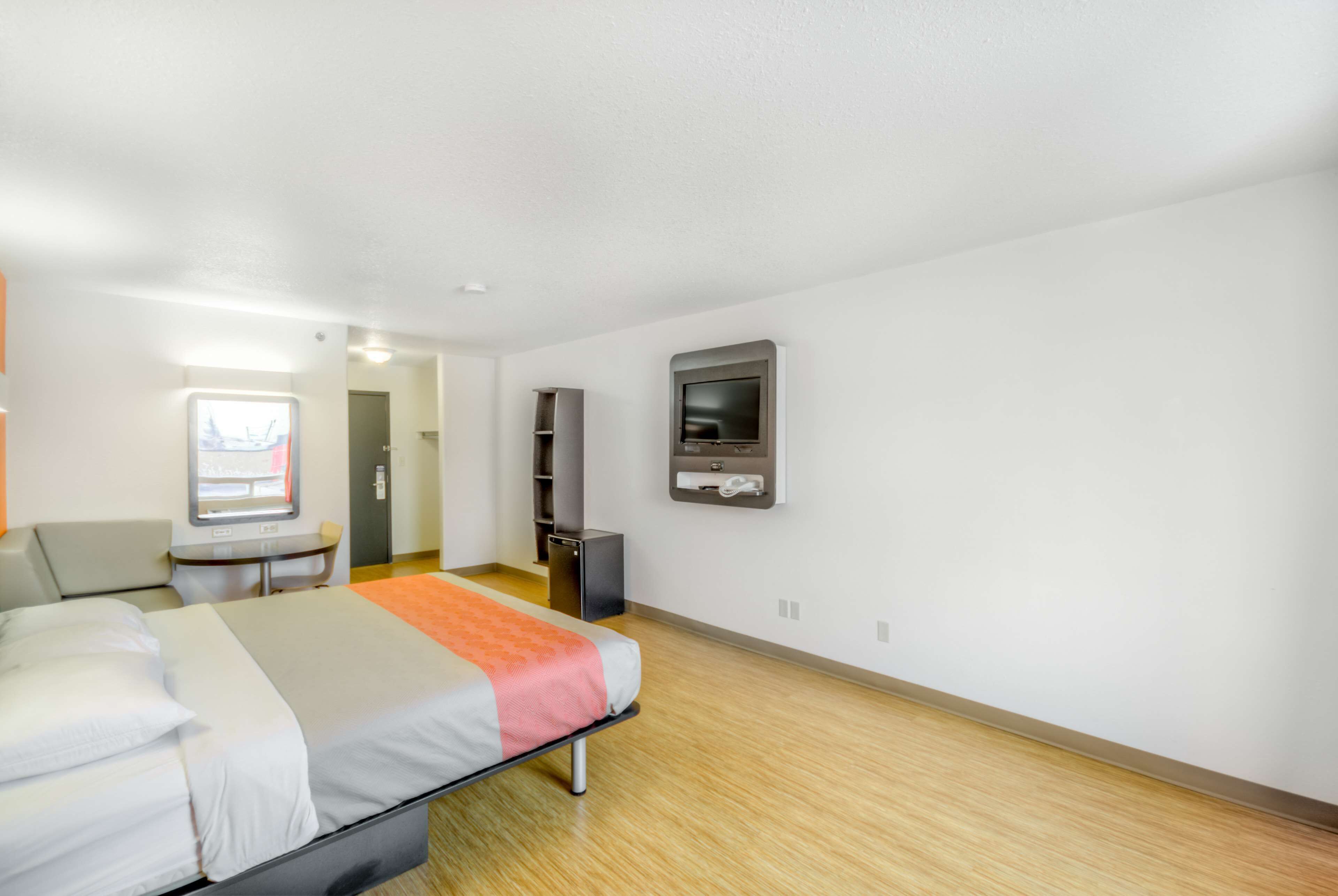 A modern hotel room with a bed, a desk, a television, and a bathroom visible in the background.