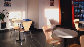 A modern indoor space with tables and chairs, a vending machine, and posters on the walls. - Motel 6 Regina, SK (Regina)