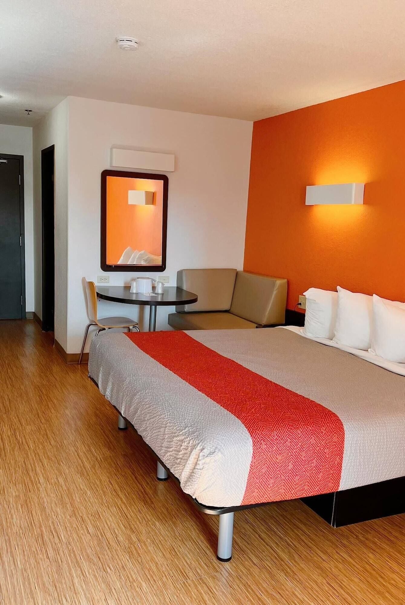Una habitación de hotel con una cama grande, un sofá, una mesita con una silla y una lámpara fijada a la pared.