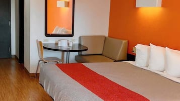 Una habitación de hotel con una cama grande, un sofá, una mesita con una silla y una lámpara fijada a la pared.