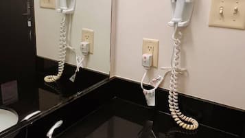 A bathroom with a white sink, a mirror, and two hair dryers mounted on the wall.