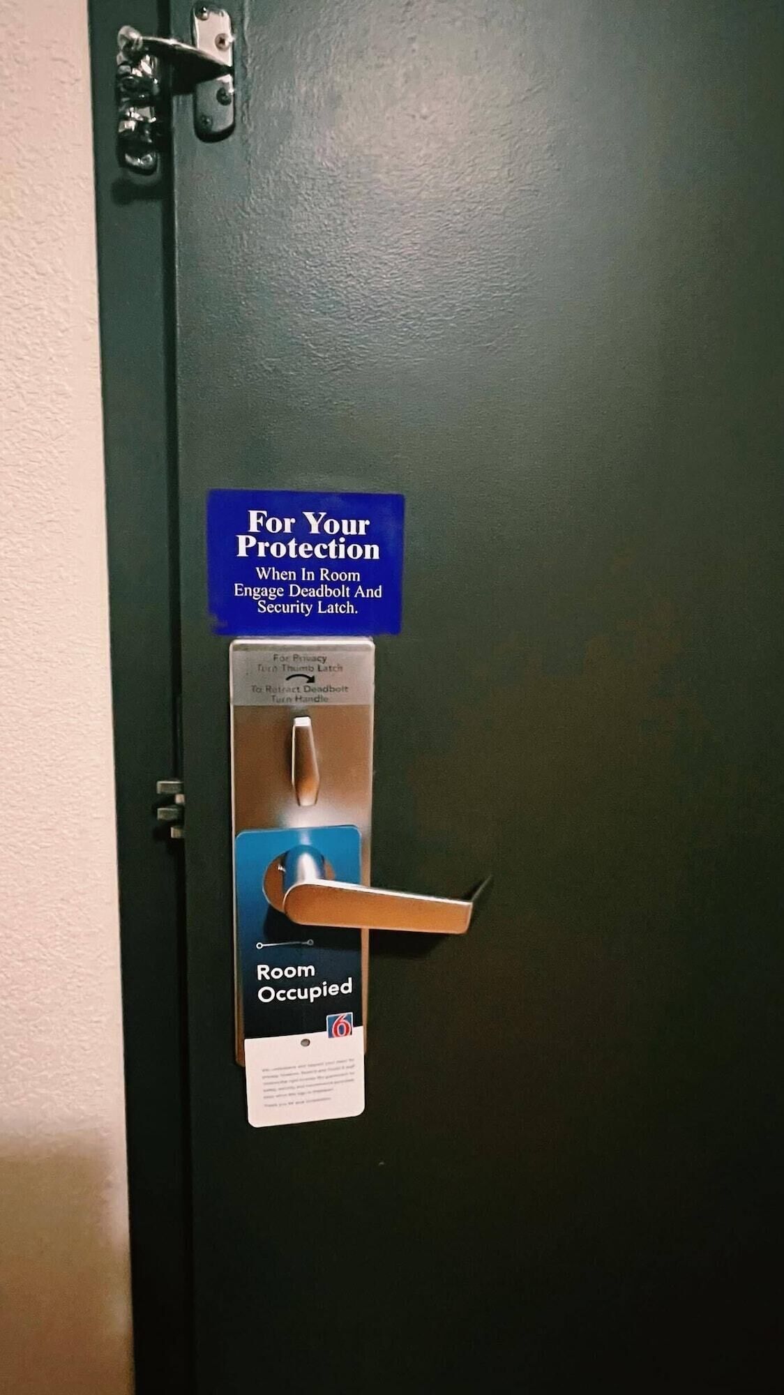 A door with a deadbolt lock and a security latch. A sign above the lock advises to engage the deadbolt and security latch for protection when in the room.