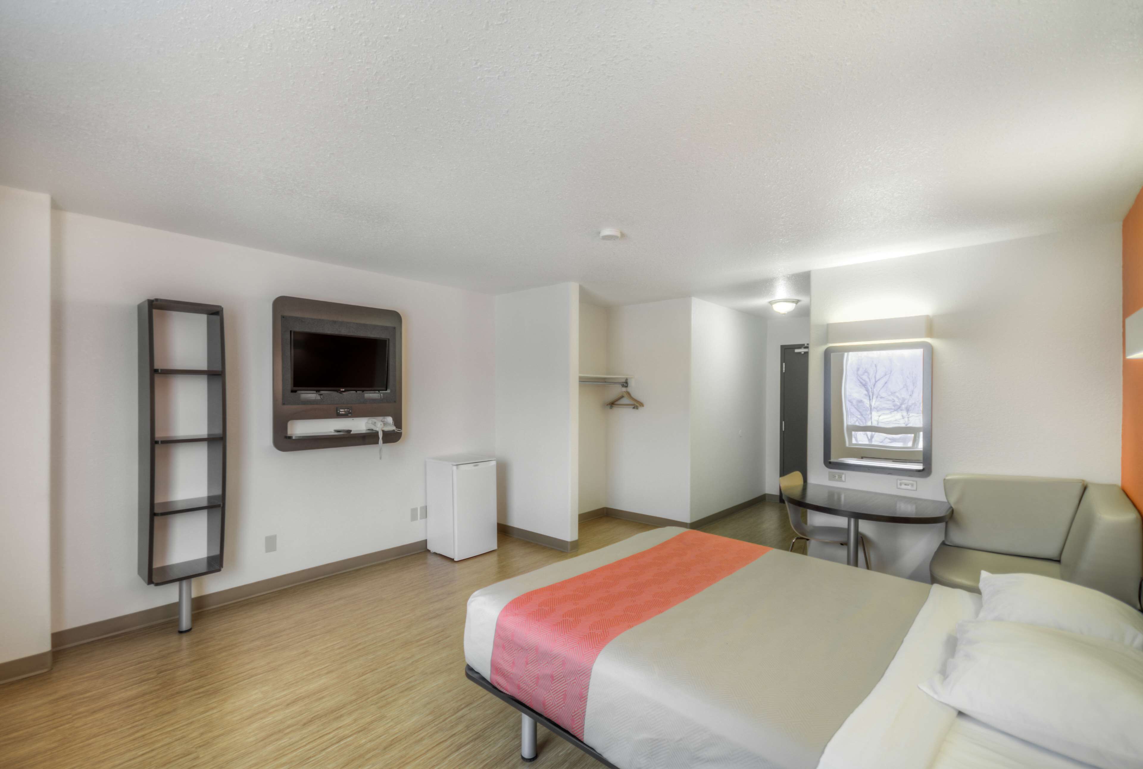 Hotellihuone, jossa on sänky, työpöytä, televisio, vaatekaappi ja pieni jääkaappi.
