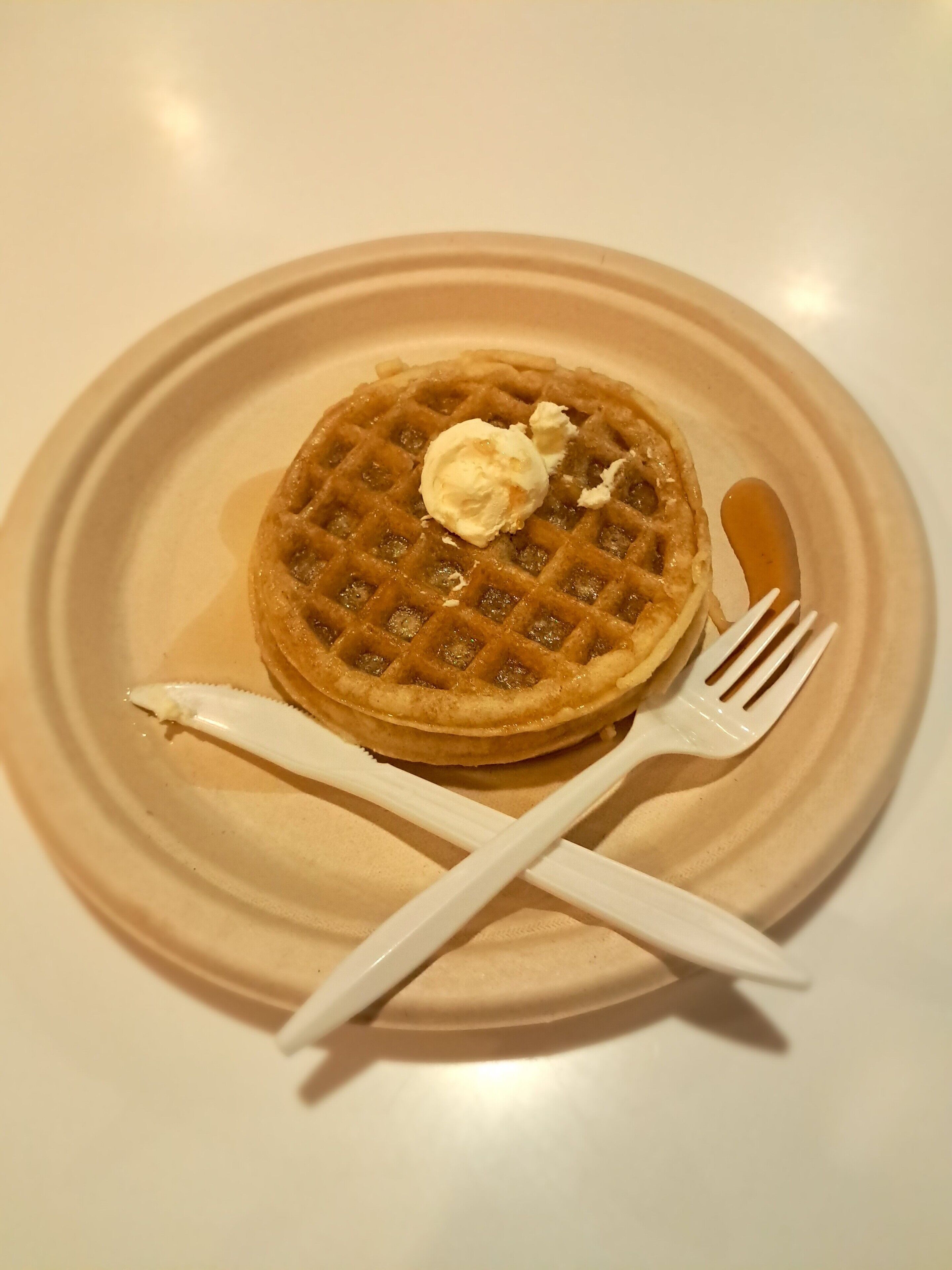 A plate with a waffle and a dollop of butter, accompanied by a fork and knife.