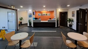 A reception area with a counter, chairs, and potted plants. - Motel 6 Regina, SK (Regina)