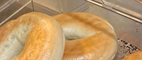 En gennemsigtig plastbeholder med et rødt værktøj, måske en paletkniv, og flere bagels med en gylden skorpe.