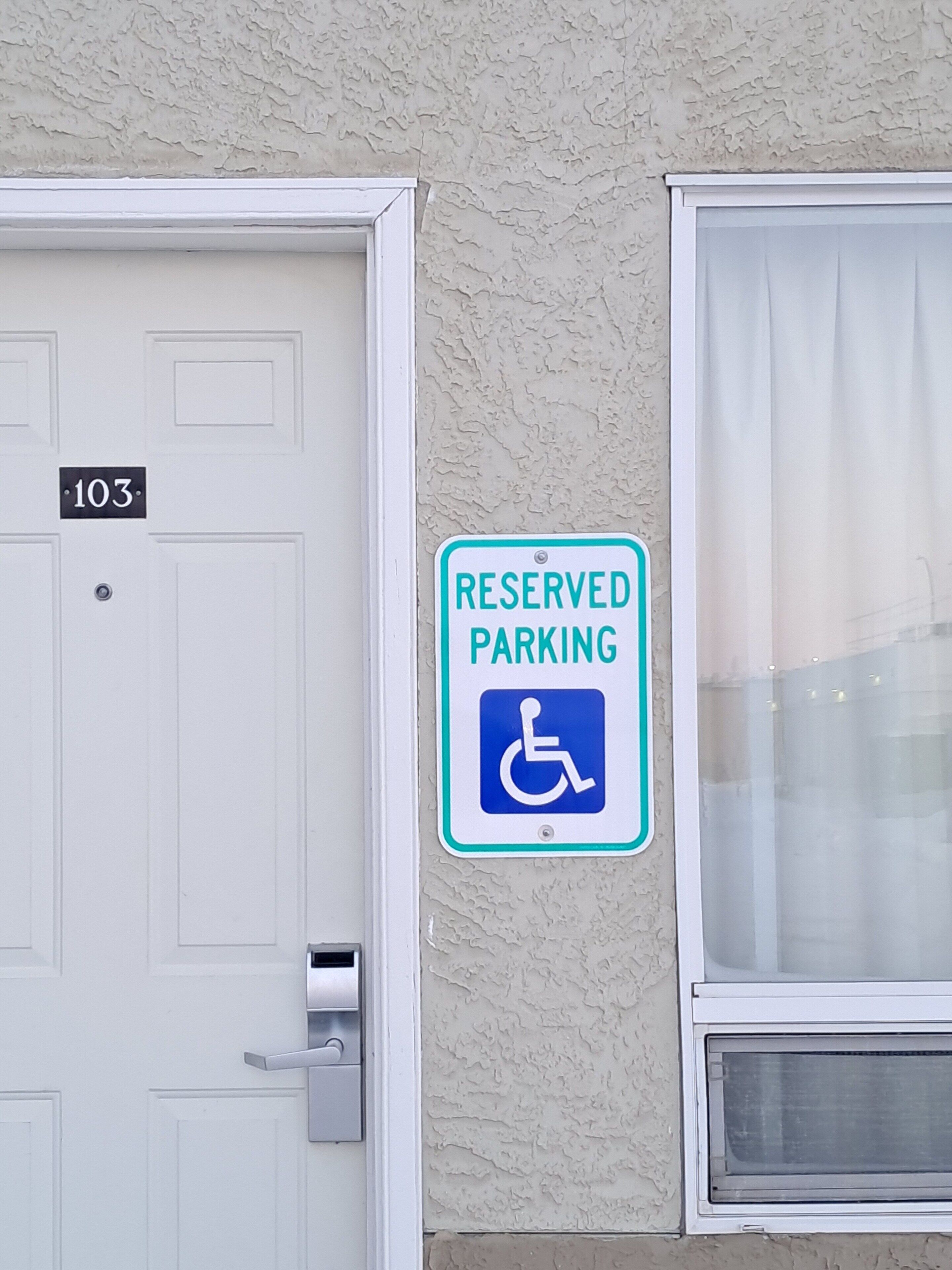 A door with the number 103 and a 'Reserved Parking' sign with a wheelchair symbol.