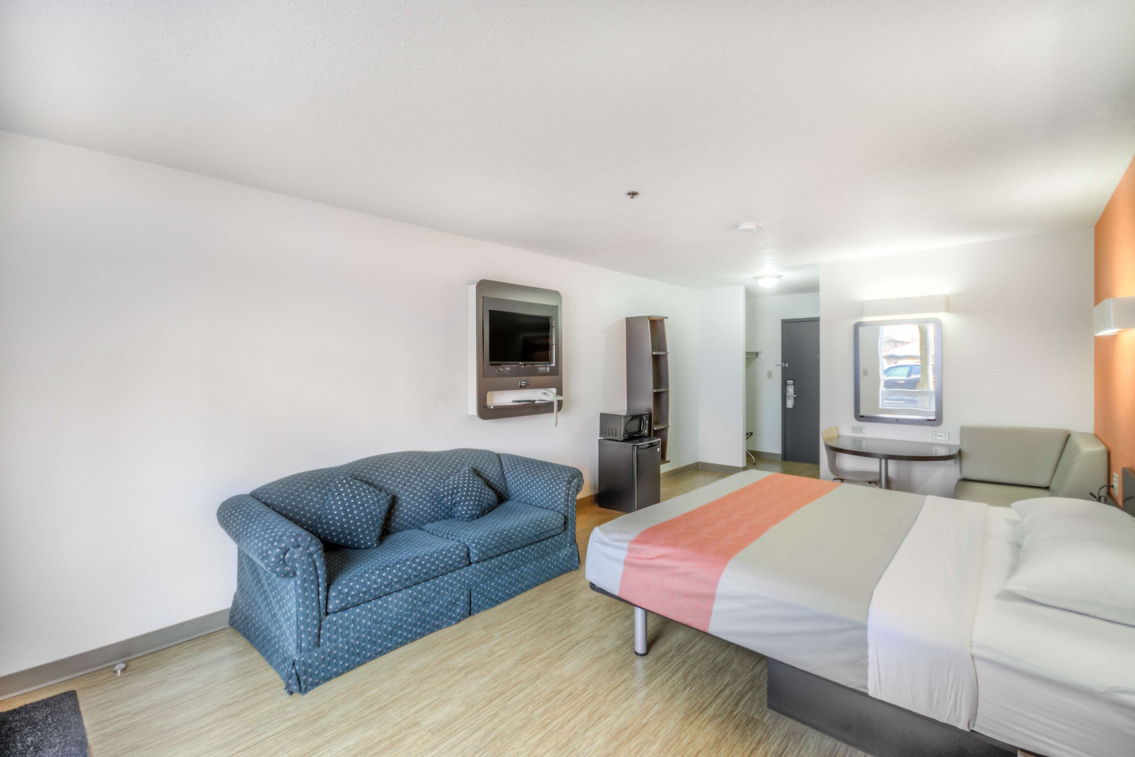 A hotel room with a bed, a sofa, a TV, a desk, and a microwave.