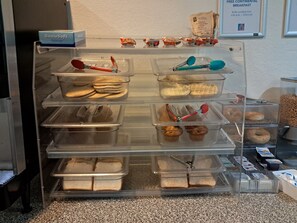 A bakery display case with various baked goods like bagels, muffins, and bread. - Motel 6 Regina, SK (Regina)