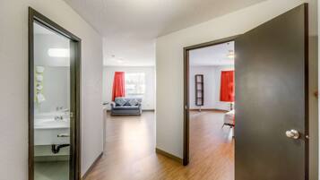 A hallway with a bathroom on the left, a grey sofa in the center, and a door leading to another room on the right.
