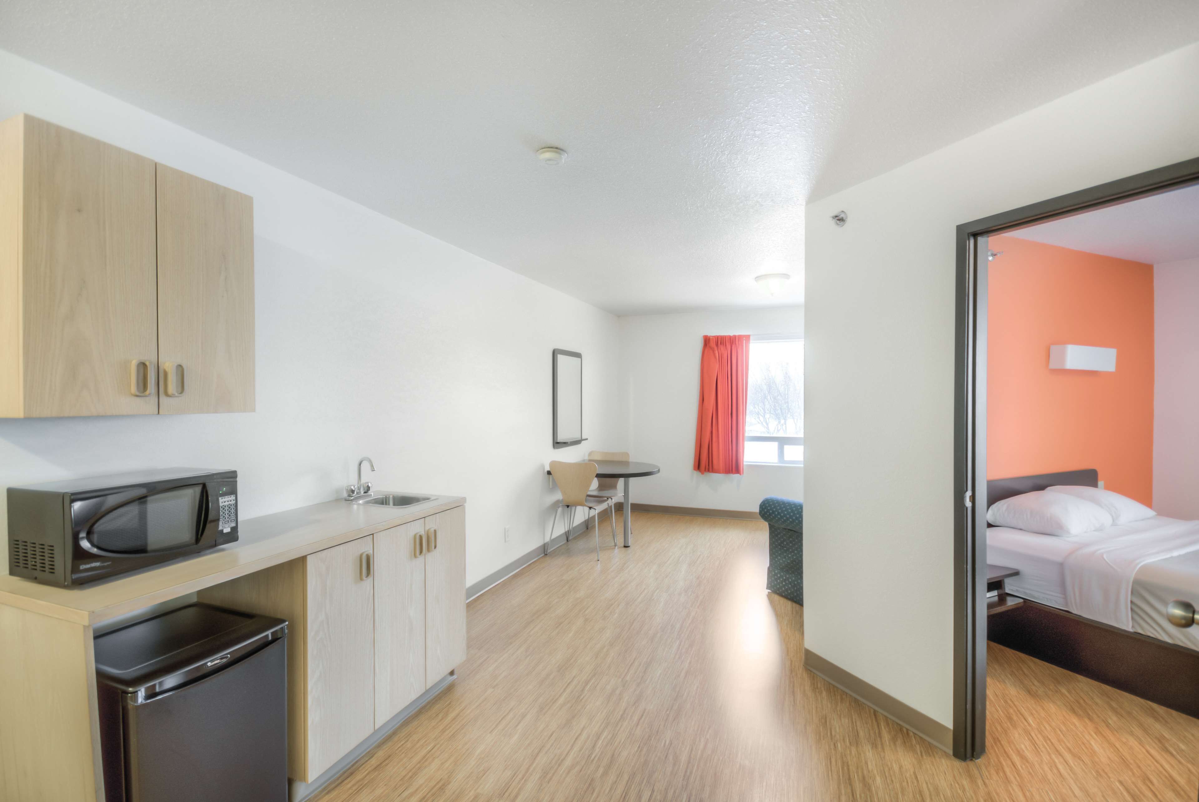 A compact hotel room with a kitchenette, a bed, and a small dining area.