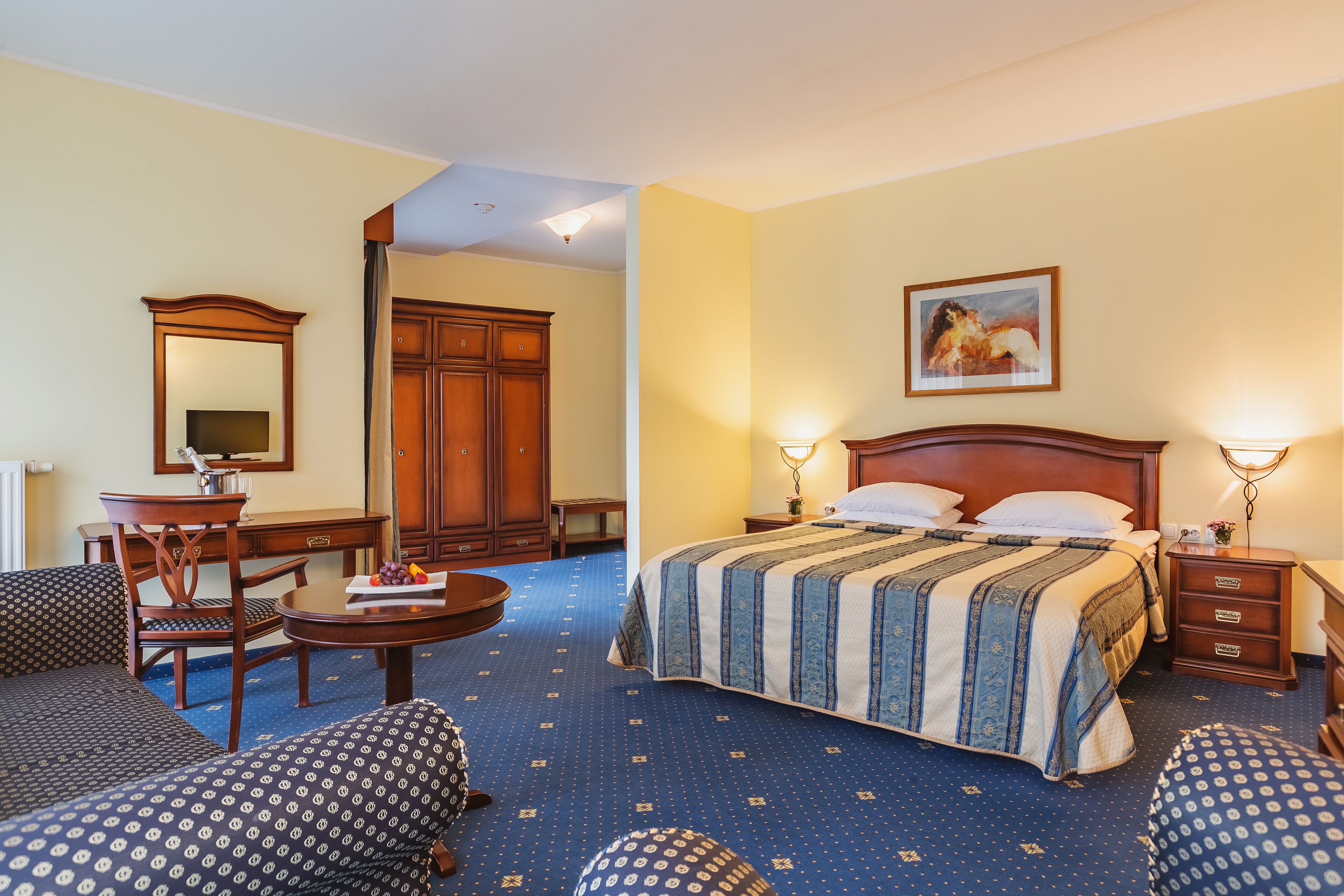 A hotel room with a large bed, a desk, a chair, and a wardrobe.