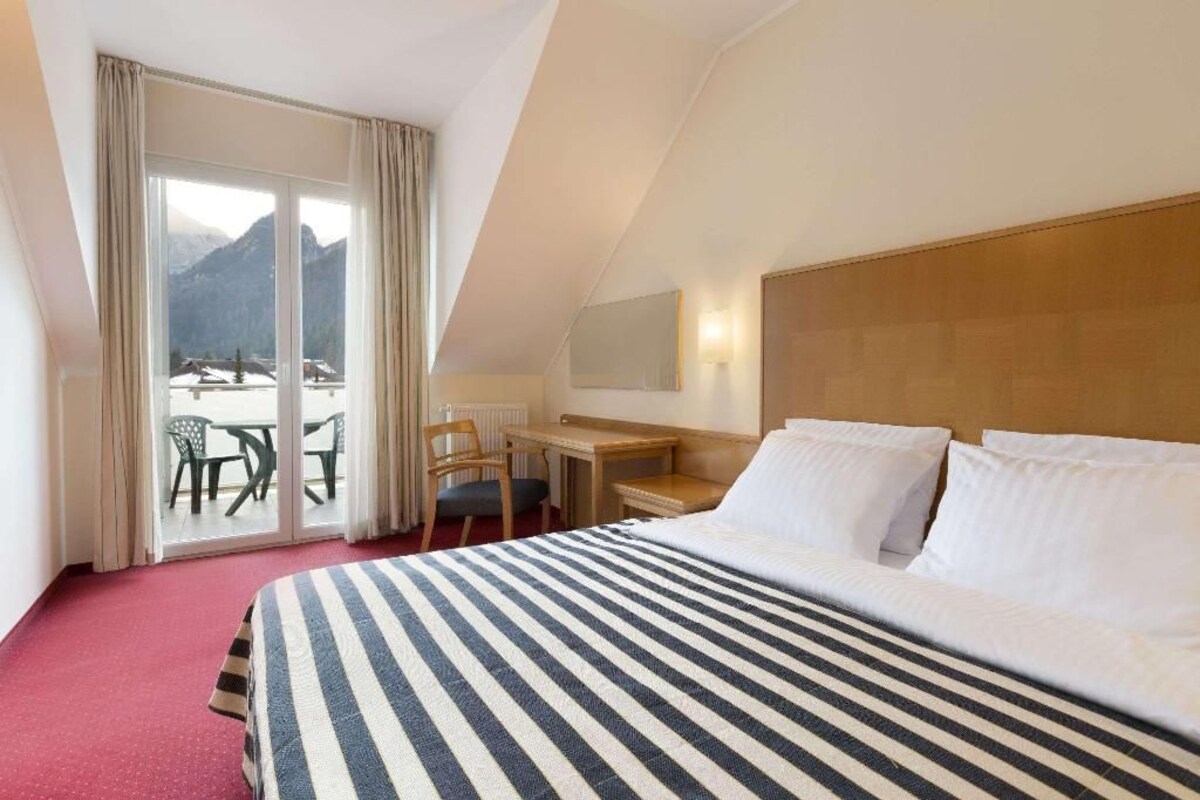 Une chambre d’hôtel avec un grand lit, un bureau et une vue sur les montagnes par la fenêtre.