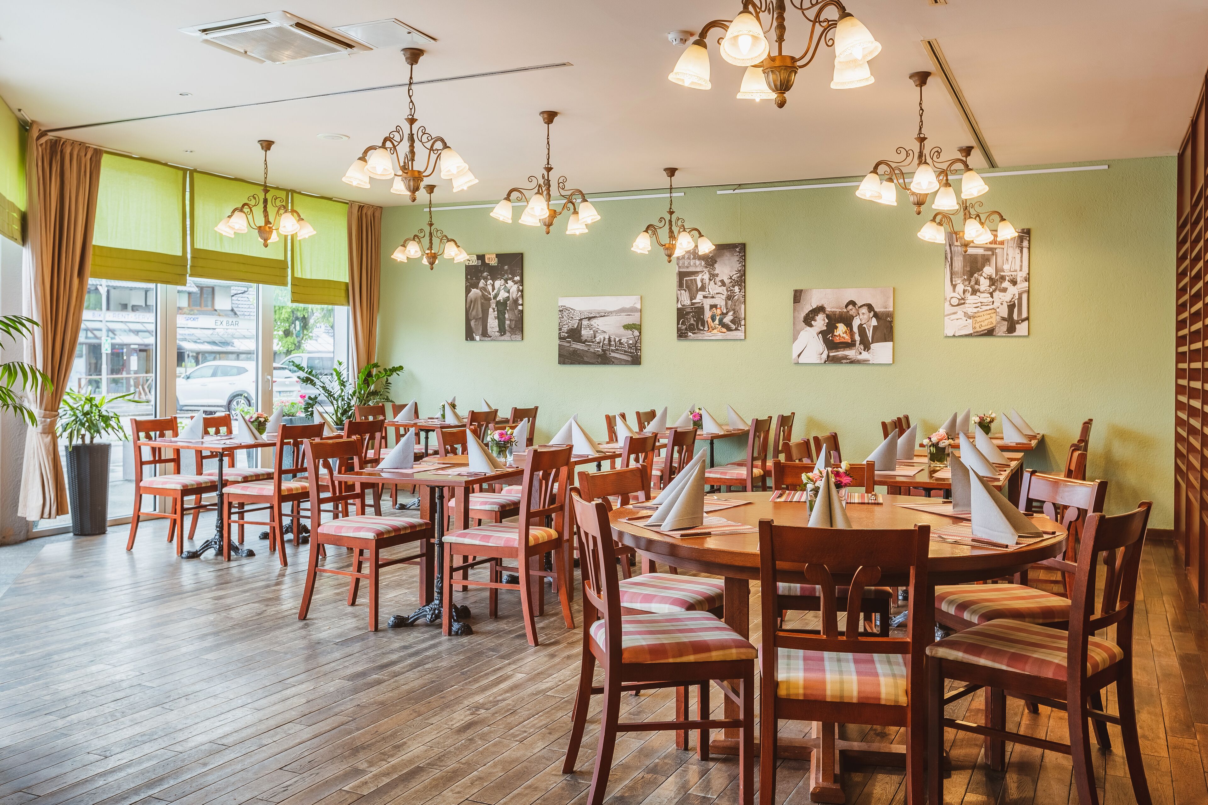 Un restaurant avec des tables et des chaises en bois, des murs verts et de nombreux luminaires suspendus.