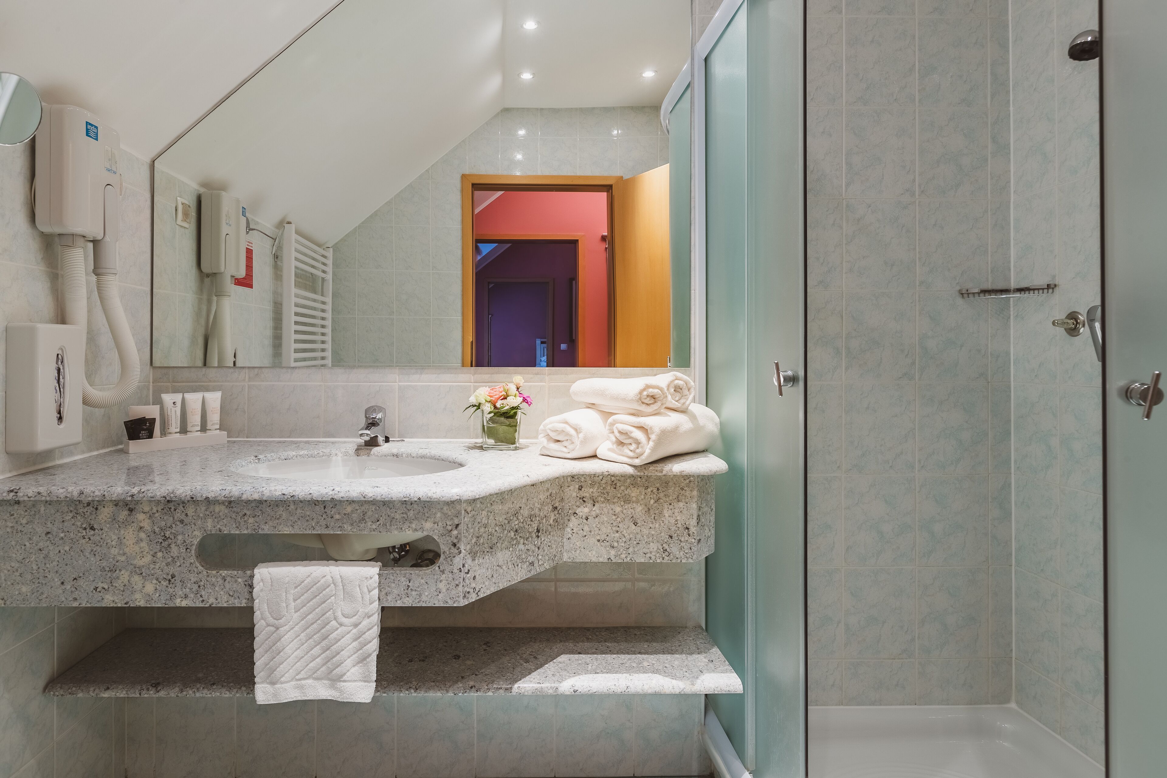 A modern bathroom with a granite countertop, a large mirror, a towel rack, and a shower area.