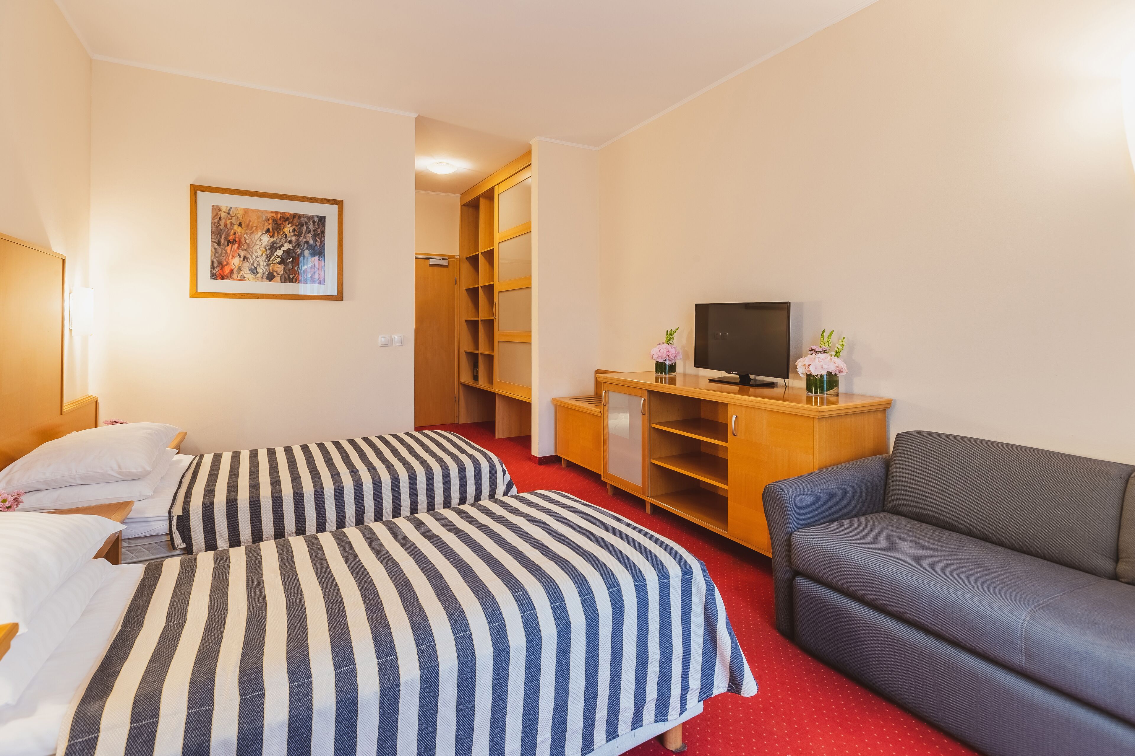 A hotel room with two beds, a sofa, a TV, and a wooden cabinet.