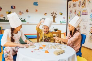 Three children playing with dough at a table in a room with colorful decorations and a whiteboard.