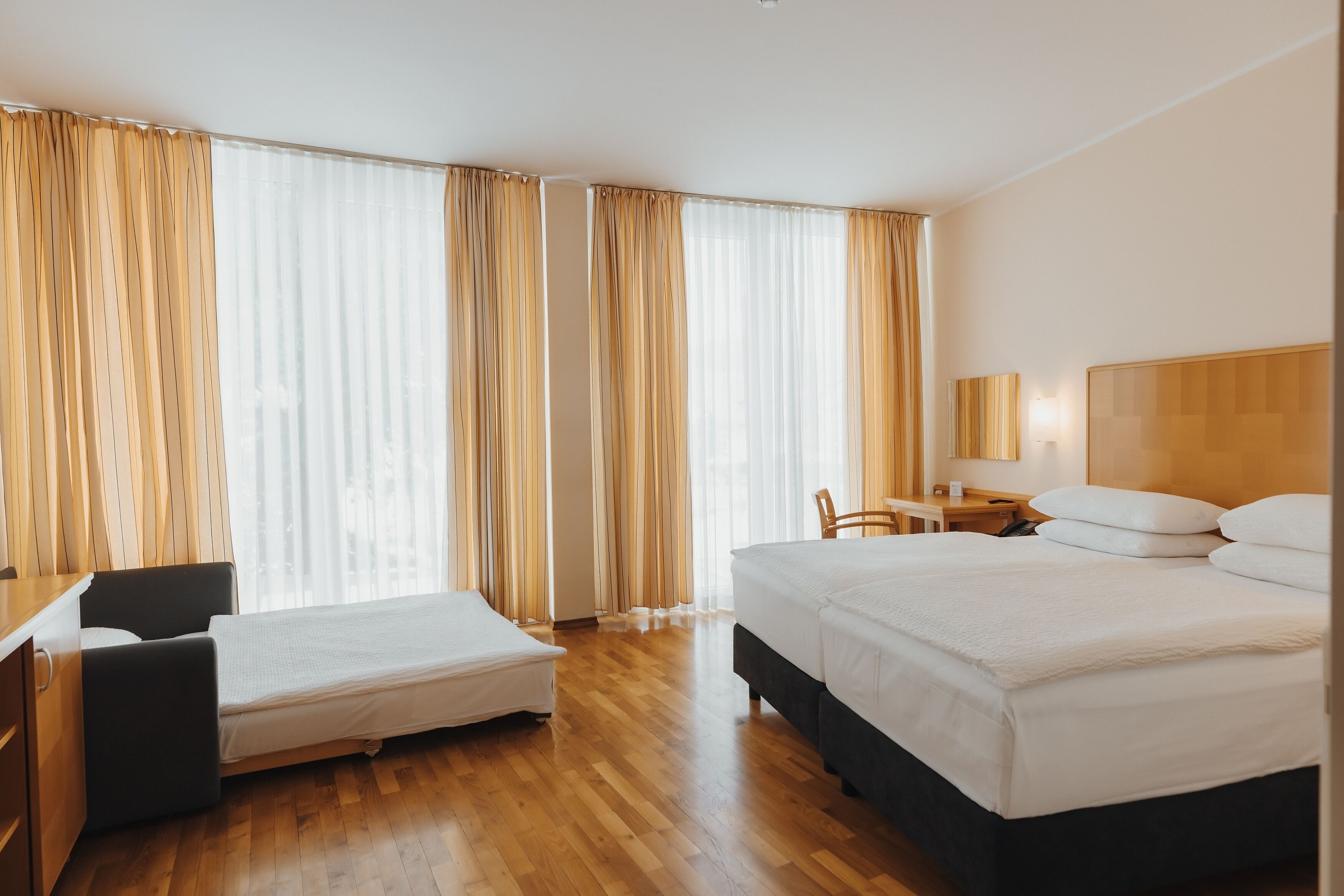 A hotel room with a bed, a desk, a chair, and a small table.