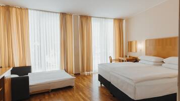 A hotel room with a bed, a desk, a chair, and a small table.