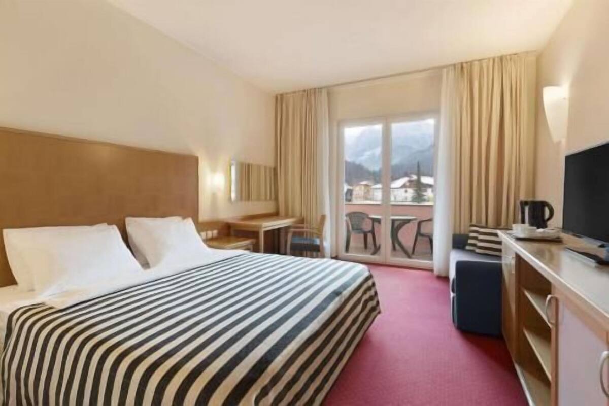Habitación de hotel con cama, escritorio, silla, televisor y vistas al exterior.