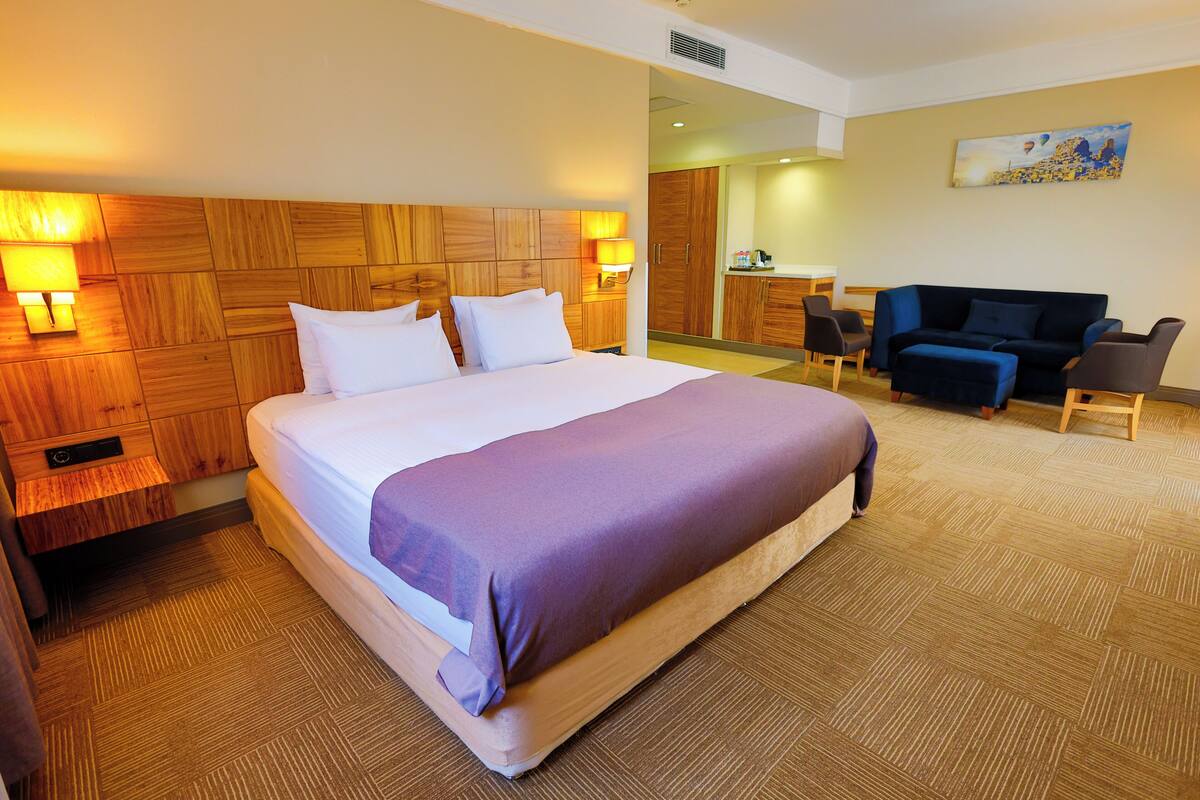 Ein Hotelzimmer mit einem großen Bett, einem hölzernen Kopfteil, einem Schreibtisch mit Stuhl und einem Sofa.