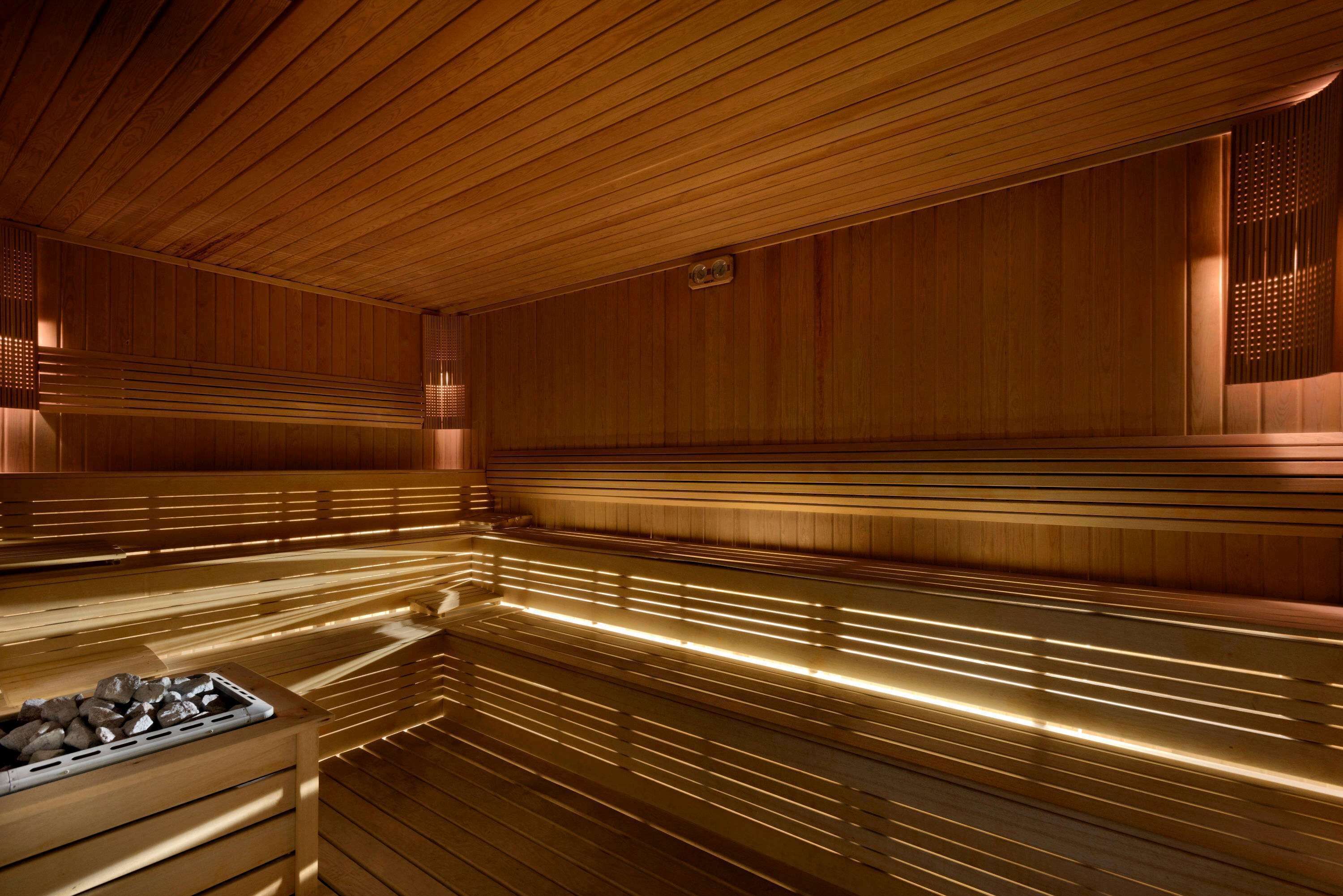 A sauna with wooden benches and a bench with a tray of stones.