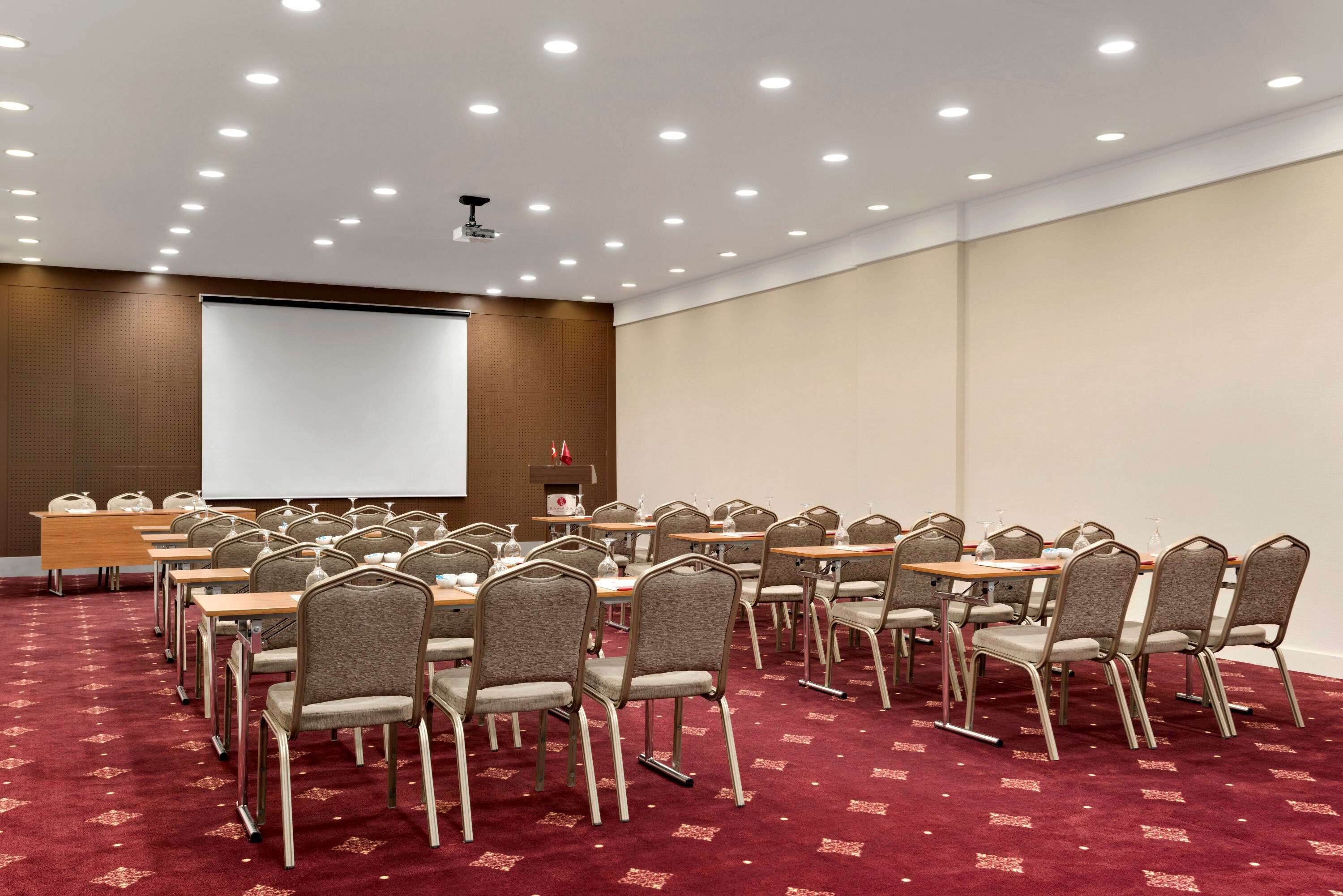 Un salón de conferencias con filas de sillas, una pantalla de proyector y suelo alfombrado.
