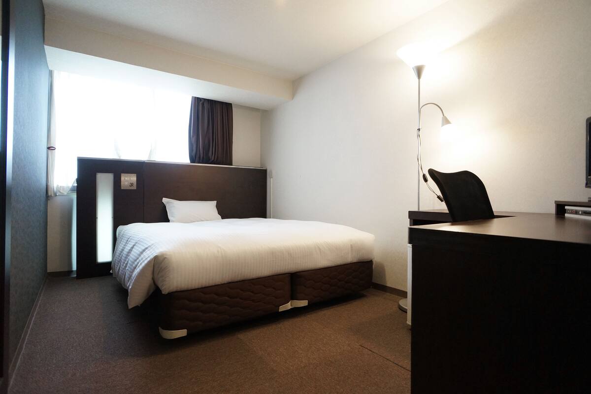 Een hotelkamer met een bed, een bureau en een lamp.