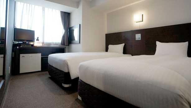 Een hotelkamer met twee bedden, een bureau met een televisie en een kleine koelkast.