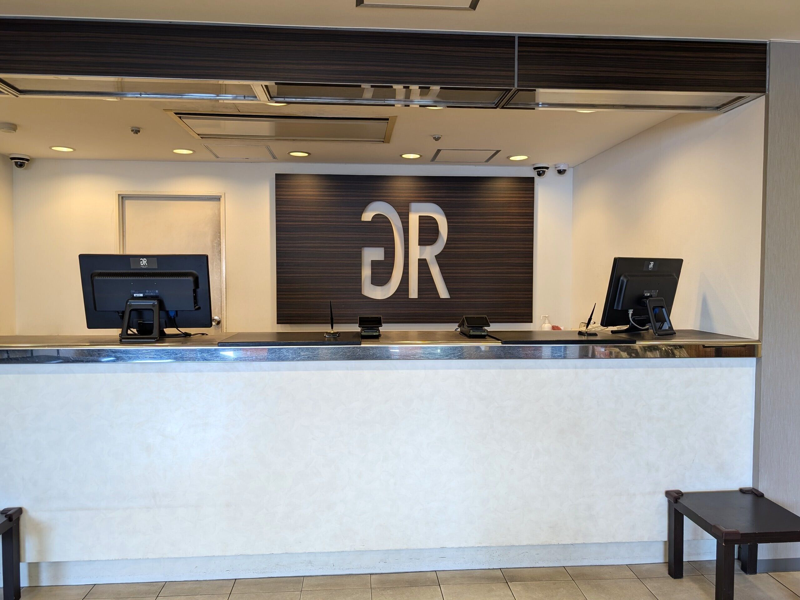 Un mostrador de recepción con dos monitores, una pared decorativa de madera con las letras 'DR' y una pequeña mesa a la derecha.