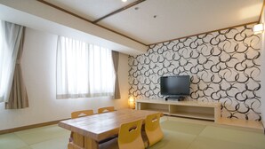 Een kamer met een houten eettafel, stoelen, een televisie op een standaard en een behang met patroon.