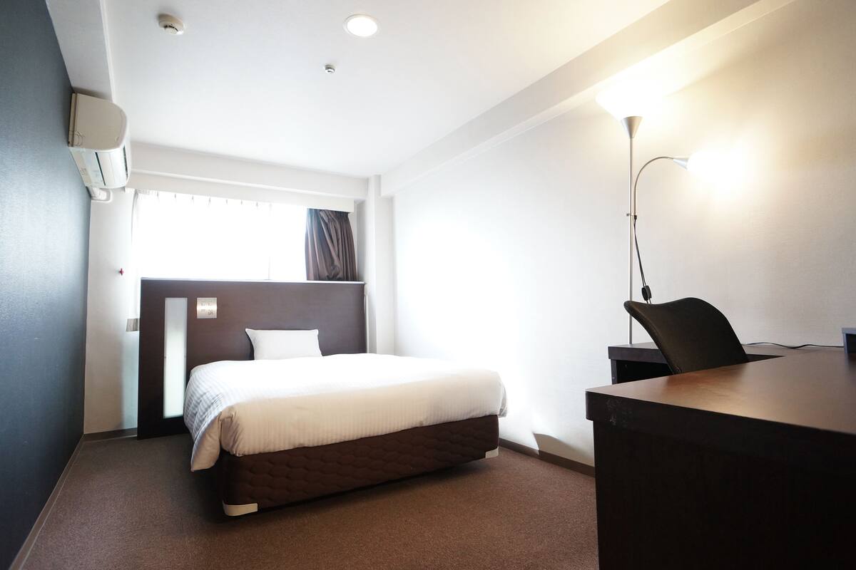 Een hotelkamer met een bed, bureau, stoel en een lamp.