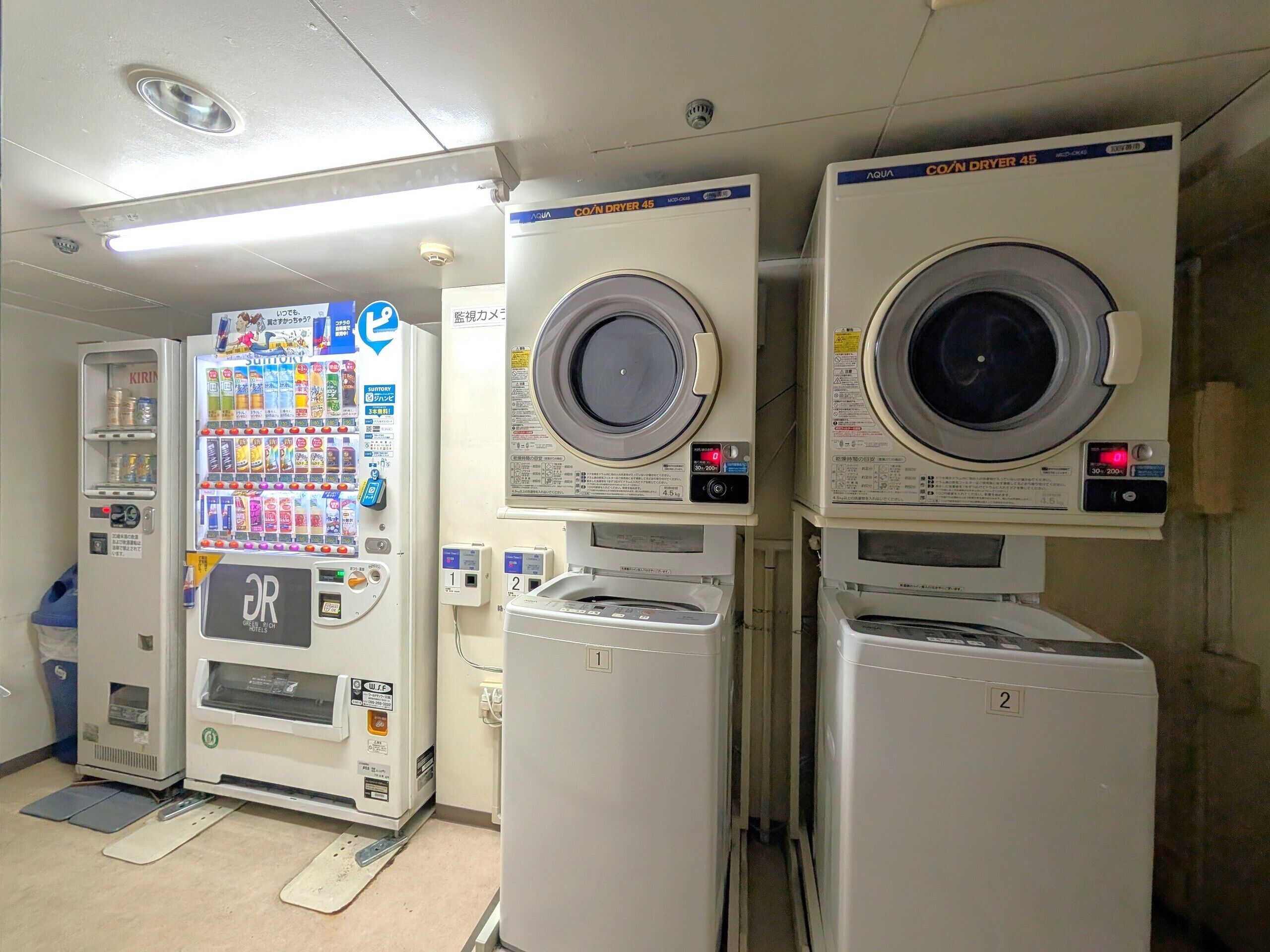 A laundromat with multiple washing machines, a vending machine, and a security camera.