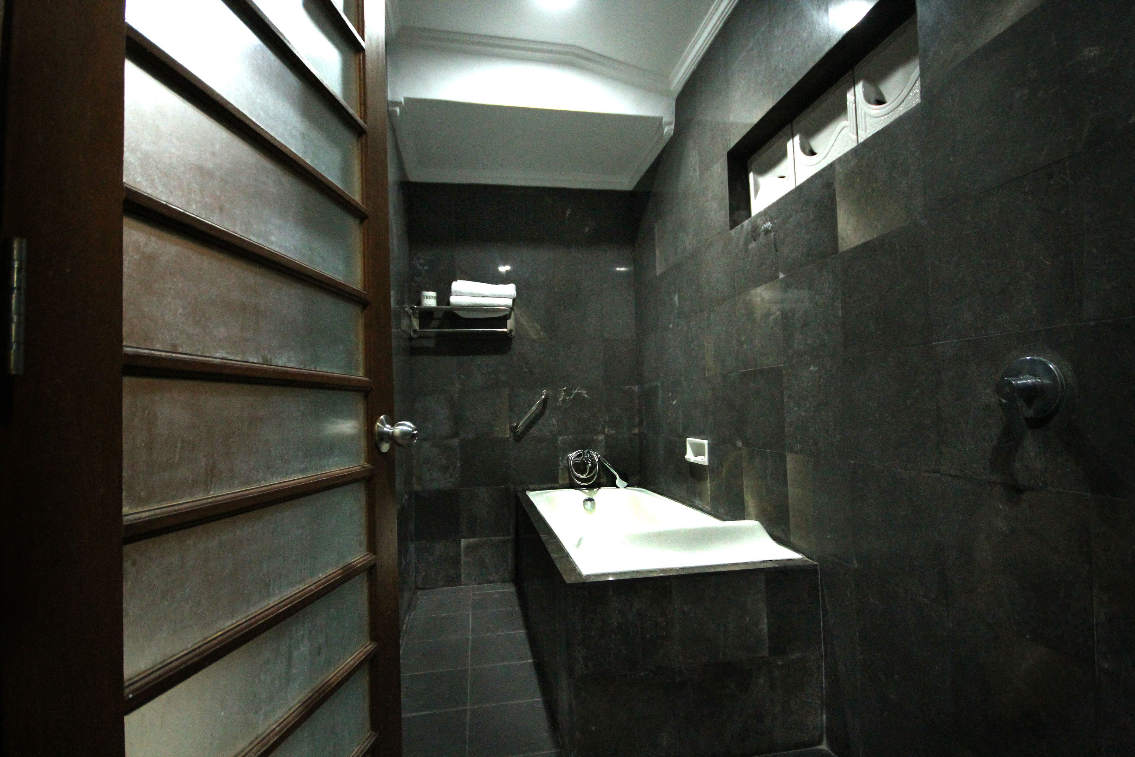 A modern bathroom with a dark tiled wall, a white sink, and a shower area.