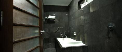 A modern bathroom with a dark tiled wall, a white sink, and a shower area.
