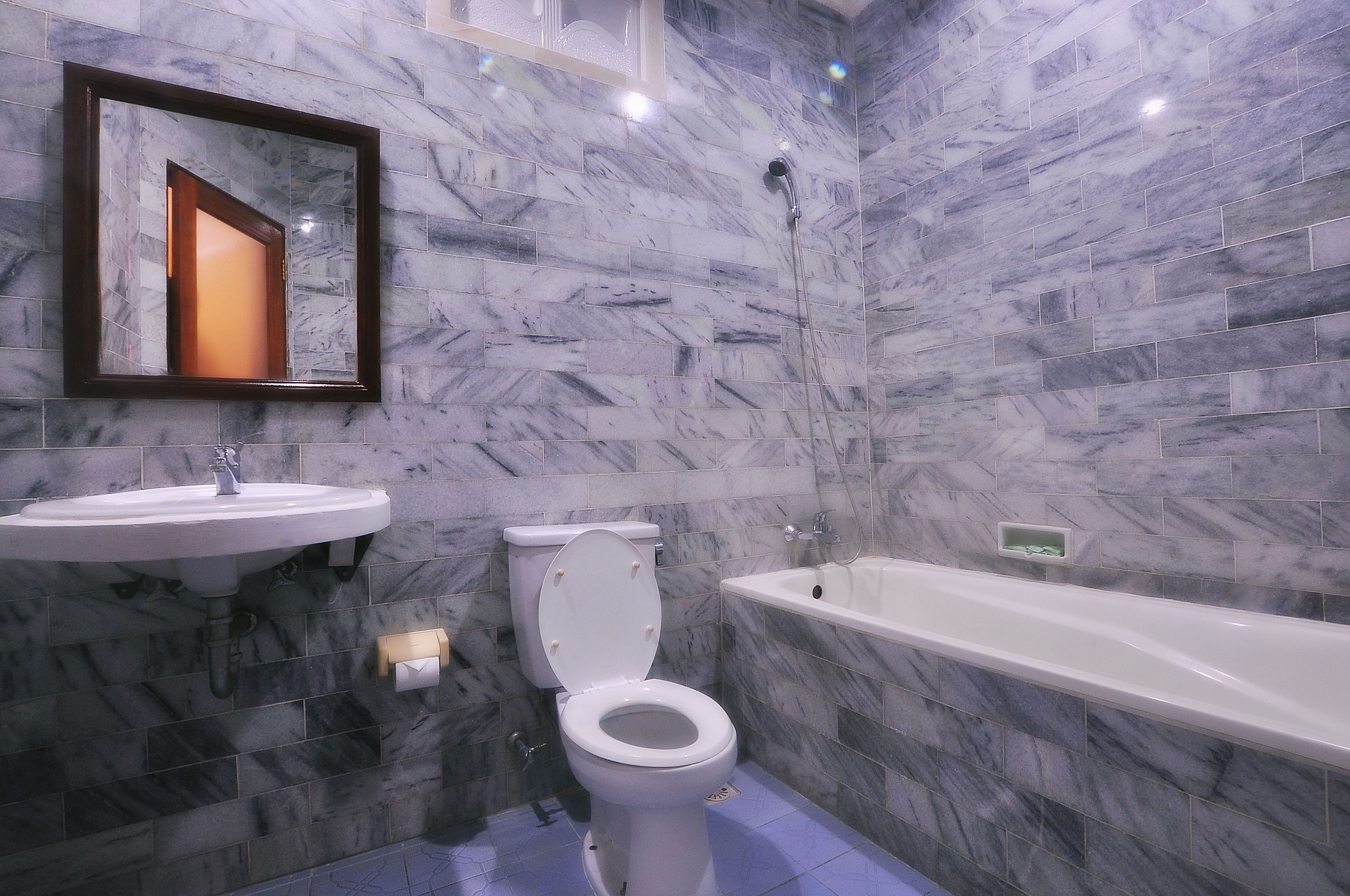 Un baño con inodoro, lavamanos y bañera, todo sobre paredes de mármol.