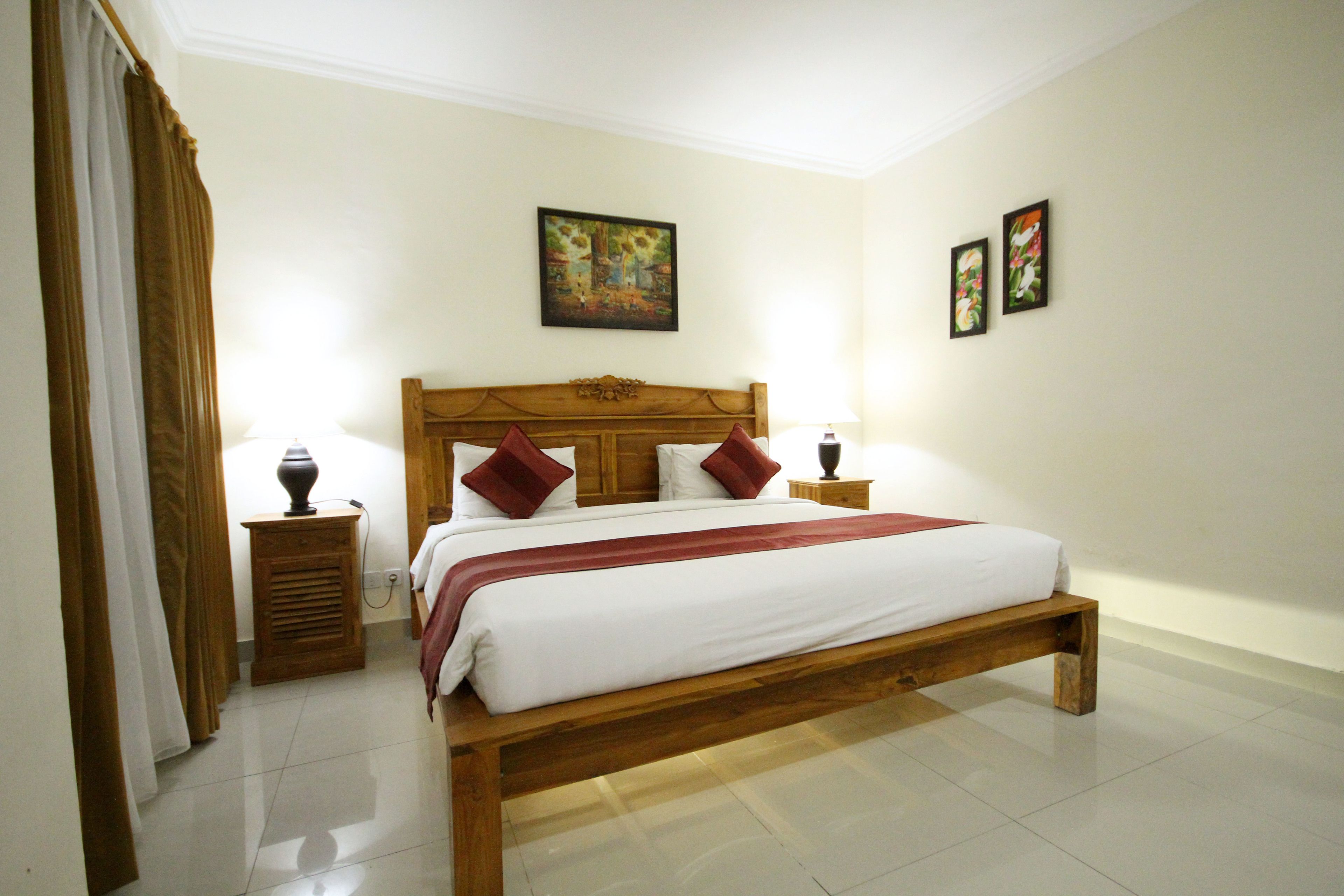A neatly made bed with a wooden headboard, two bedside tables with lamps, and a painting on the wall.