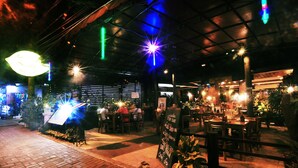An outdoor restaurant with tables and chairs, illuminated by various lights. - Swastika Guest House (Denpasar)