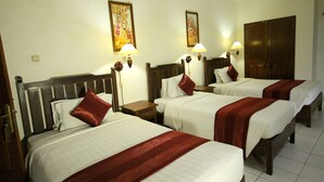 A hotel room with three beds, each with white bedding and red accents, wooden headboards, and bedside lamps. - Swastika Guest House (Denpasar)