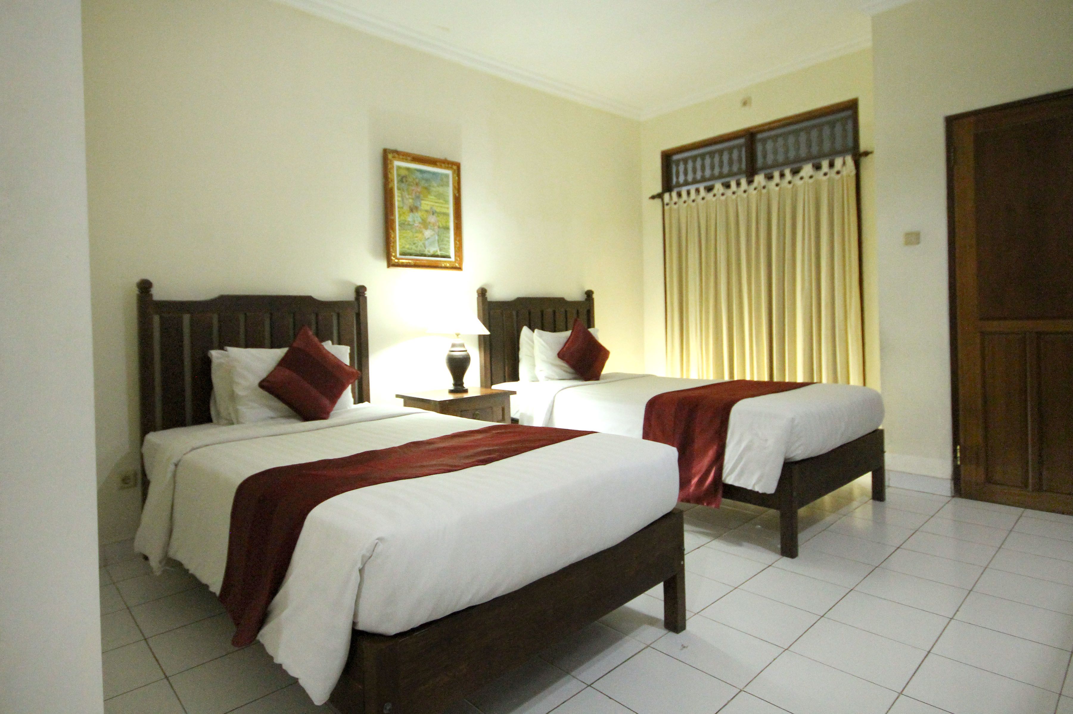 A hotel room with two single beds, a nightstand with a lamp, a painting on the wall, and a window with curtains.