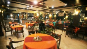 A restaurant with multiple tables and chairs, a bar area, and potted plants. - Swastika Guest House (Denpasar)